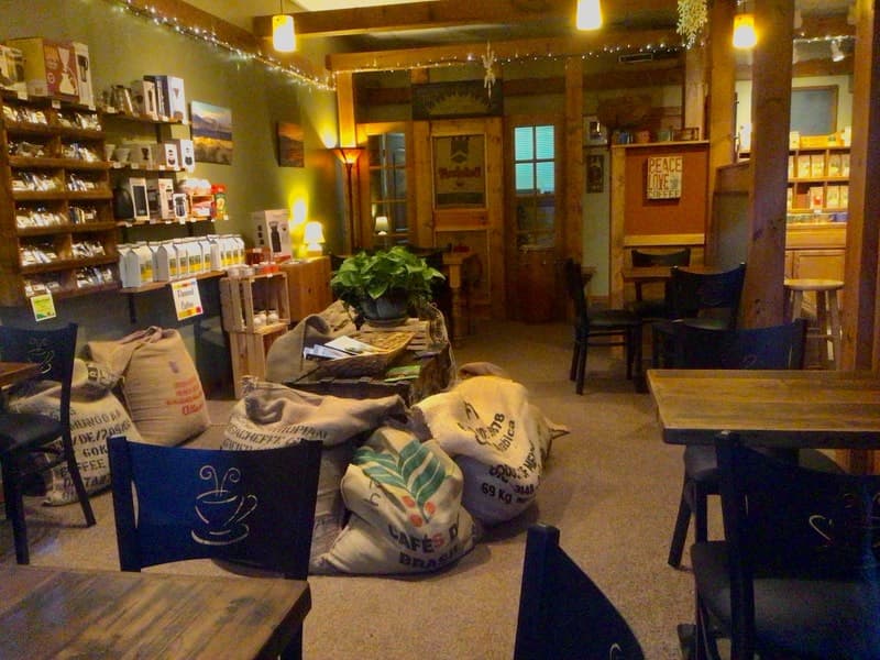 Inside the Lakewood coffee house: wood beams, string lights, tables, and burlap sacks of green coffee